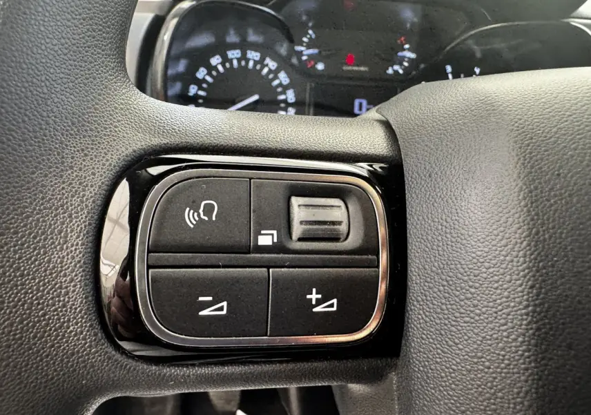 Gros plan sur les commandes du volant noir de la Citroën C3 beige PureTech 83, avec tableau de bord en arrière-plan flou.