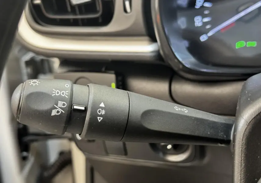 Gros plan sur la commande des phares et clignotants à gauche du volant d’une Citroën C3 beige, tableau de bord partiellement visible.
