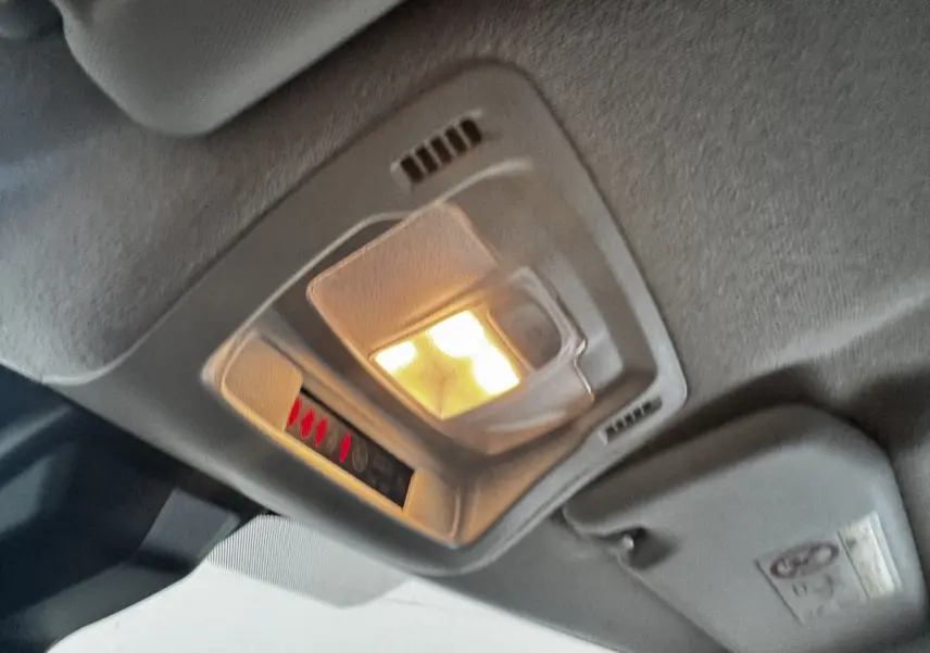 Plafonnier intérieur allumé vu en gros plan dans une Citroën C3 beige, avec pare-soleil et ciel de toit gris.