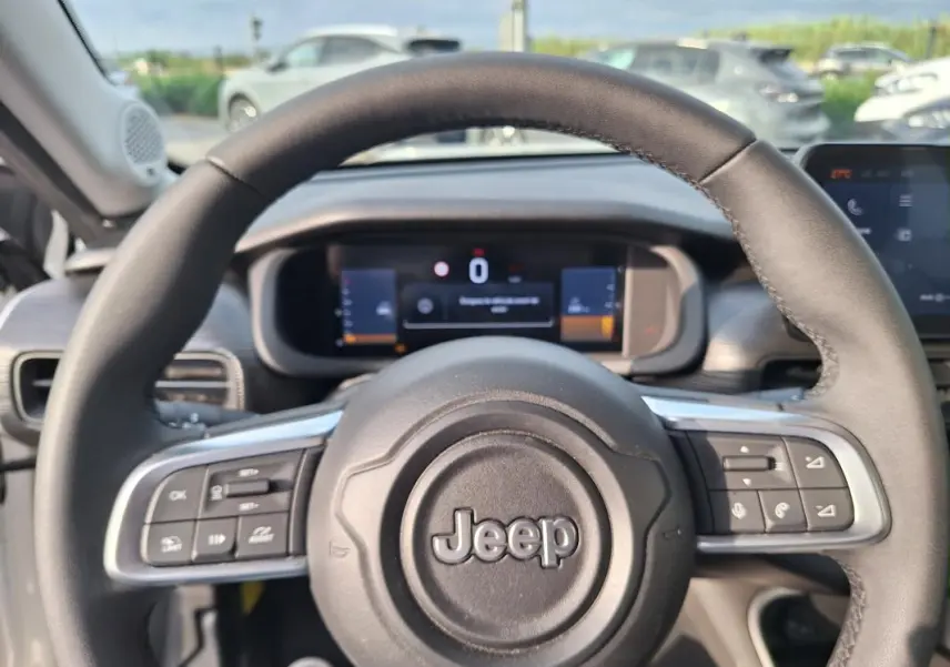 Vue rapprochée du volant Jeep Avenger blanc 2025, avec commandes intégrées et tableau de bord numérique en arrière-plan.