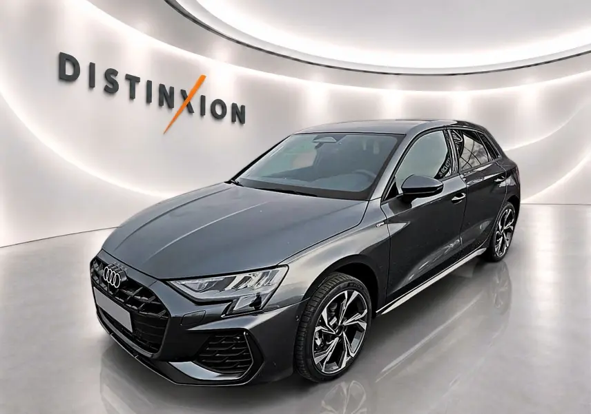 Audi A3 Sportback gris Daytona vue 3/4 avant droit dans un showroom lumineux avec jantes alu graphiques.