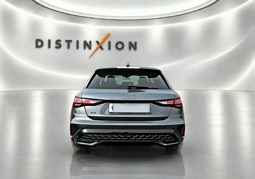 Vue arrière d'une Audi A3 Sportback 2026 gris Daytona, avec feux LED et diffuseur noir dans un showroom lumineux.