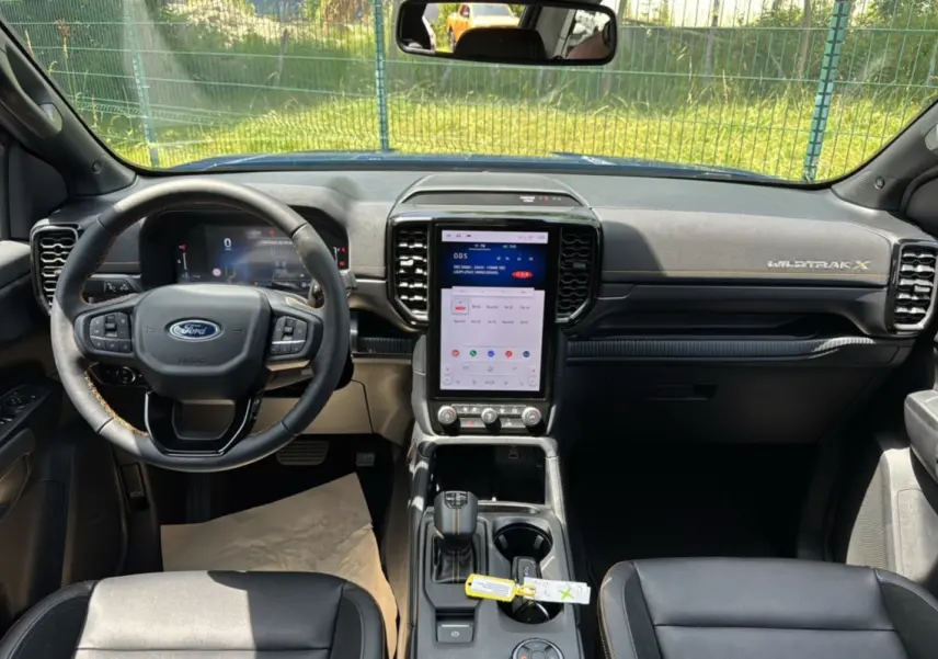 Vue intérieure avant du Ford Ranger Wildtrak X avec tableau de bord noir, volant cuir multifonctions et écran tactile vertical.