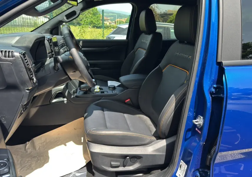 Vue intérieure côté conducteur du Ford Ranger Wildtrak X bleu lightning, sièges noirs avec surpiqûres orange et tableau de bord moderne.