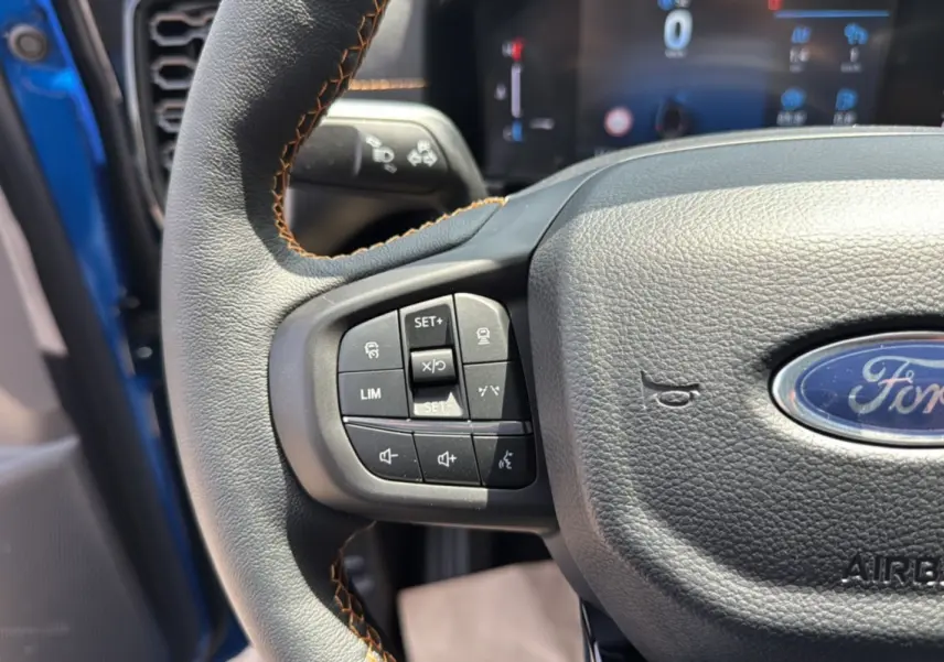 Gros plan sur le volant cuir multifonctions du Ford Ranger bleu lightning, avec commandes de régulateur et logo Ford visible.