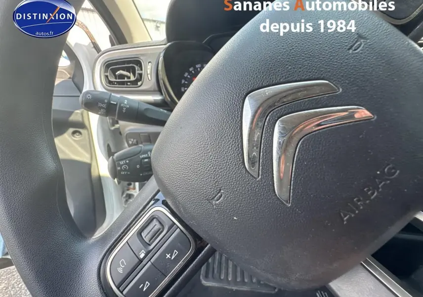 Gros plan sur le volant Citroën C3 blanc, mettant en valeur les commandes audio intégrées et le tableau de bord partiel.