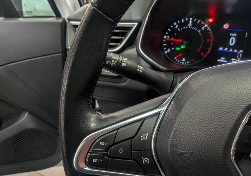 Gros plan sur le volant côté gauche de la Renault Clio V Business 2020, avec commandes de régulateur et tableau de bord allumé.
