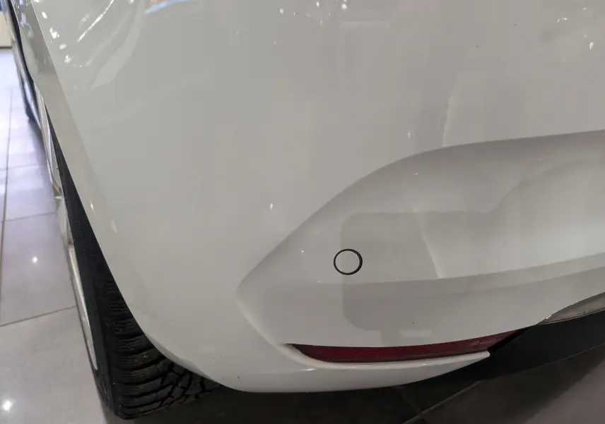 Gros plan sur le pare-chocs arrière droit blanc glacier d'une Renault Clio V Business 2020 avec capteur de recul visible.