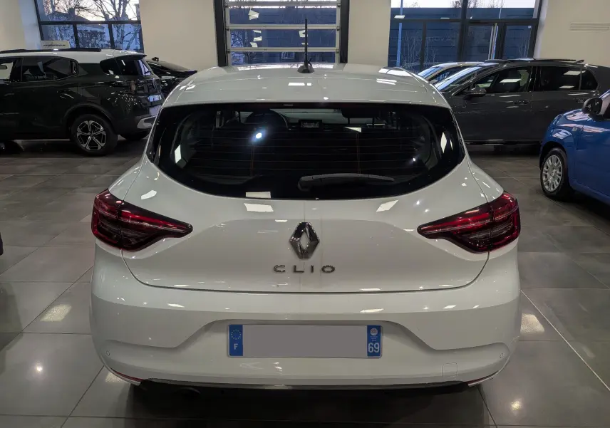 Vue arrière d'une Renault Clio V Blanc Glacier en intérieur, avec feux arrière LED et logo Renault bien visibles.