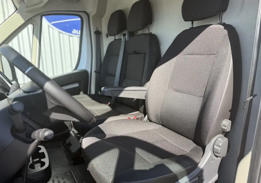 Vue intérieure côté conducteur de l’Opel Movano Fourgon blanc, montrant les sièges en tissu noir avec accoudoir.