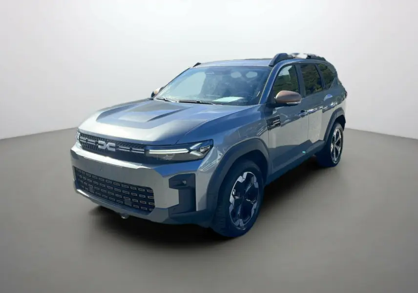 Dacia Bigster gris schiste en 3/4 avant droit avec jantes alu noires et barres de toit visibles.