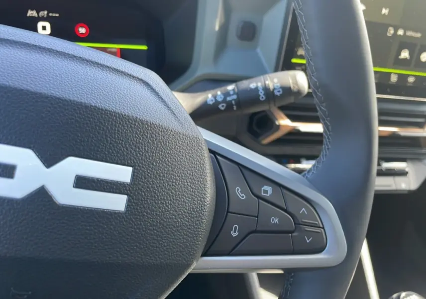 Gros plan sur le volant cuir noir du Dacia Bigster 2025, avec commandes multifonctions et tableau de bord digital en arrière-plan.