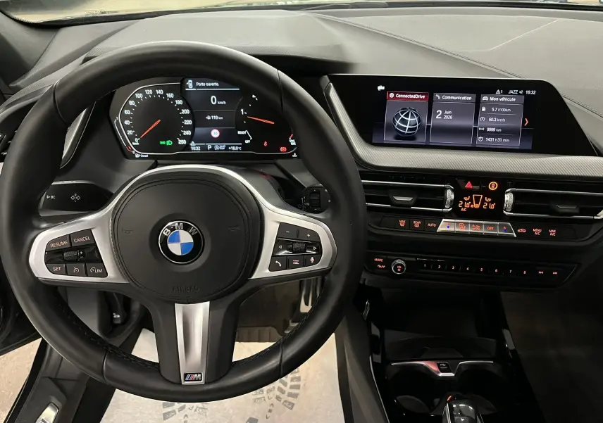 Vue intérieure centrée sur le volant M sport noir avec commandes, tableau de bord digital et écran multimédia BMW Série 1 F40.