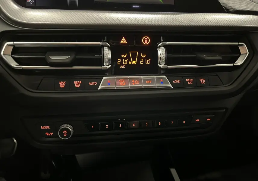 Vue rapprochée du tableau de bord noir de la BMW Série 1 F40 118dA, mettant en valeur les commandes de climatisation et audio rétroéclairées.