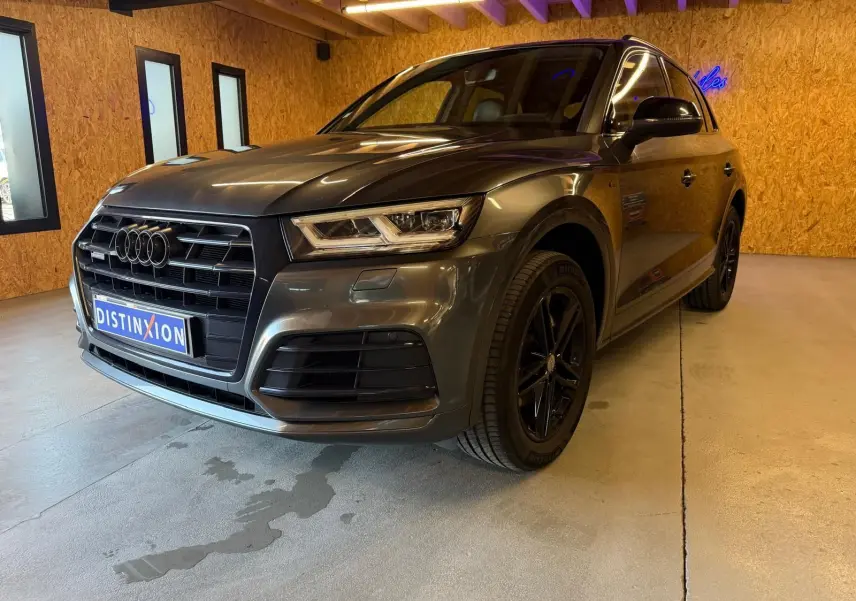 Audi Q5 Sportback gris en vue 3/4 avant droit, avec jantes noires et calandre imposante dans un intérieur en bois.