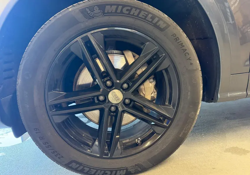 Gros plan sur la roue avant droite noire avec jante Audi en alliage du Q5 Sportback gris 2019.