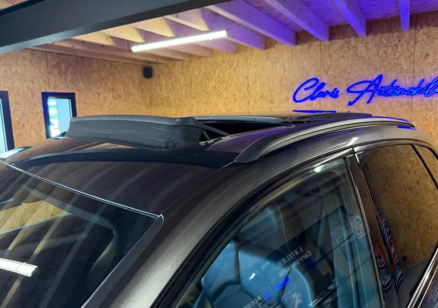 Toit ouvrant ouvert sur le côté gauche d’un Audi Q5 Sportback gris, avec barres de toit visibles en intérieur.