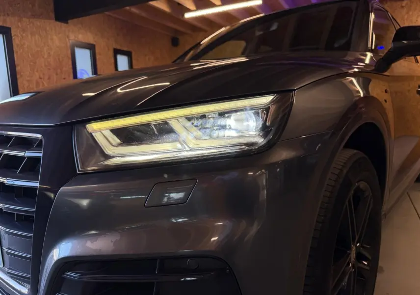 Gros plan sur l'avant droit gris d'un Audi Q5 Sportback 2019 avec phares LED allumés et jante noire visible.