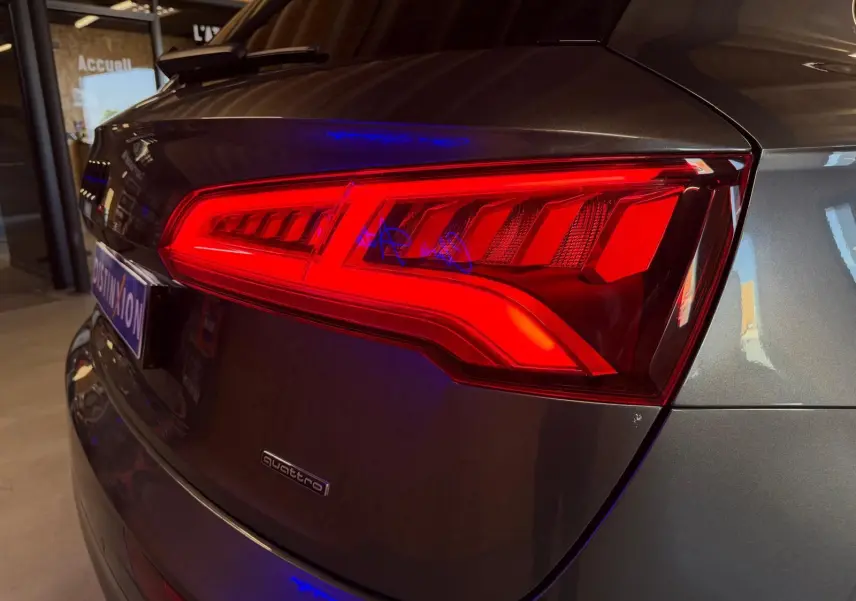 Gros plan sur le feu arrière droit rouge d’un Audi Q5 Sportback gris métallisé, avec logo quattro visible sur le hayon.