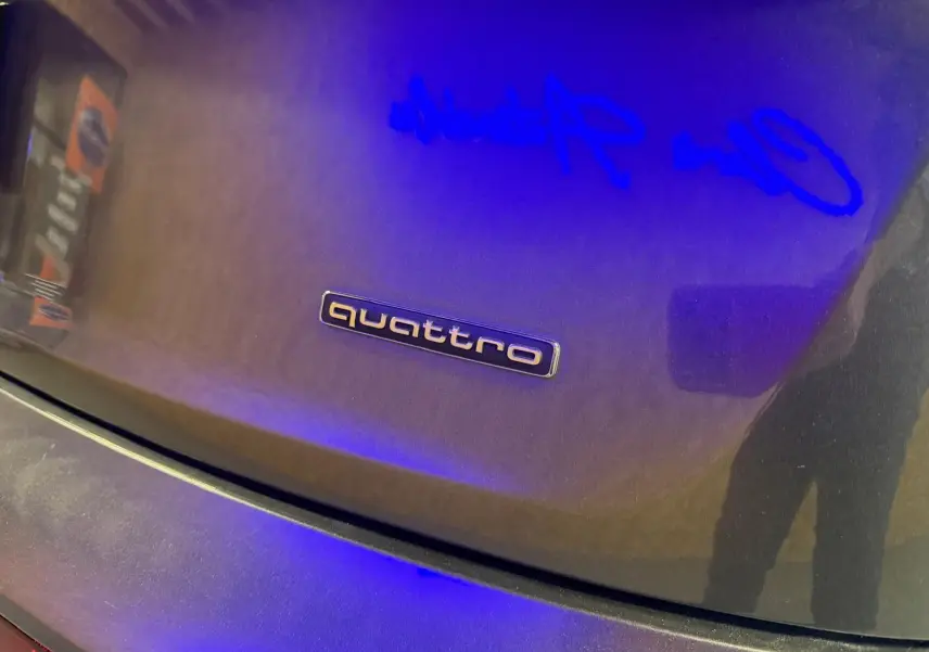 Gros plan sur le logo quattro sur la malle arrière grise d’un Audi Q5 Sportback, reflet bleu visible.
