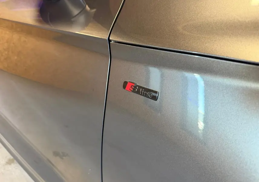 Détail du logo S line sur la portière côté gauche d’un Audi Q5 Sportback gris métallisé.