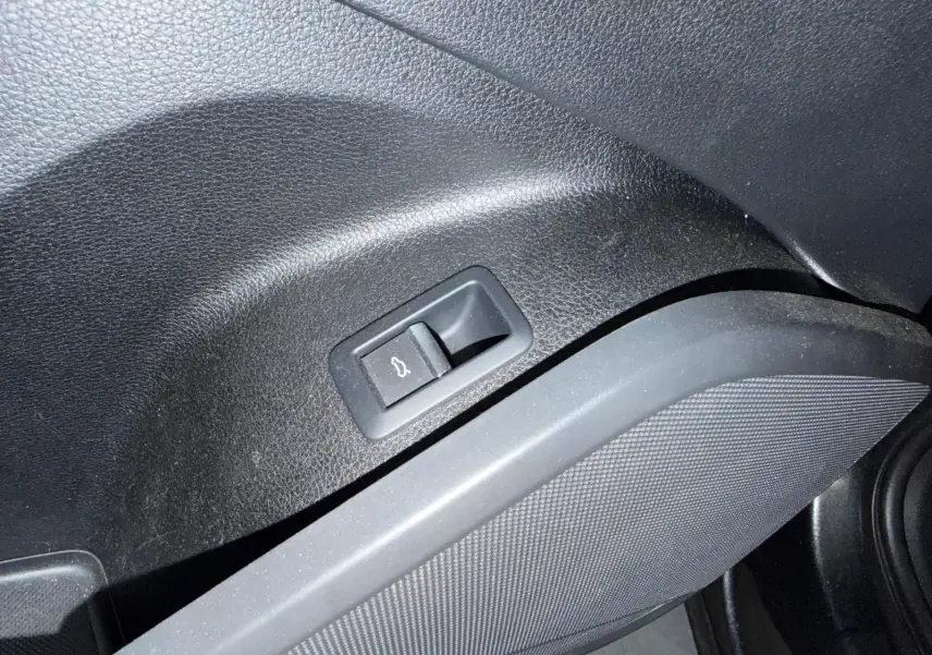 Bouton d'ouverture du hayon intégré dans le panneau intérieur noir côté gauche de l'Audi Q5 Sportback gris.
