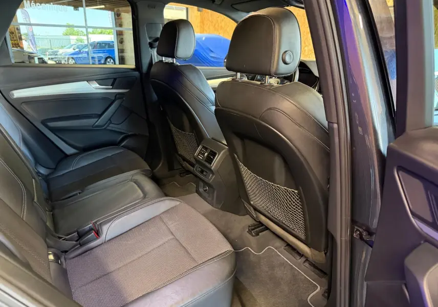 Vue intérieure arrière droite de l’Audi Q5 Sportback gris, sièges en cuir noir avec finitions tissu et rangement filets au dos des sièges avant.
