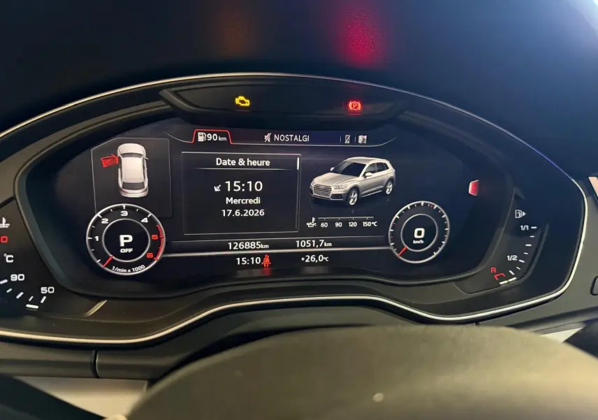 Tableau de bord numérique de l'Audi Q5 gris, affichant la date, l'heure et un véhicule en vue 3/4 avant.
