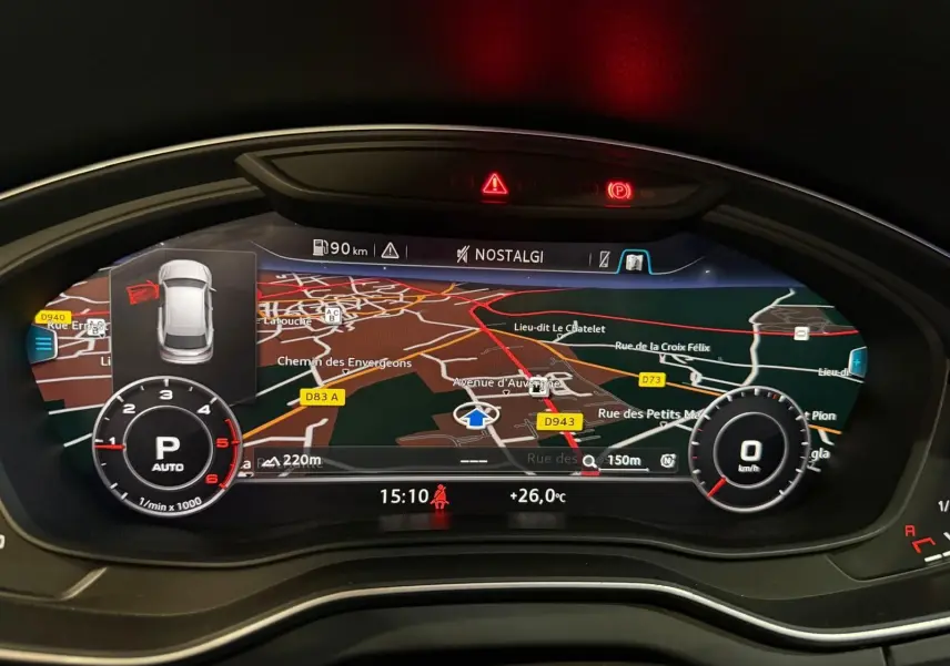 Vue rapprochée du tableau de bord numérique de l'Audi Q5 gris, affichant la navigation et les indicateurs de vitesse et régime.