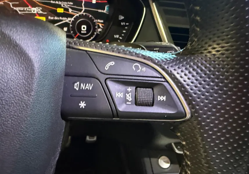 Gros plan sur les commandes du volant côté gauche de l’Audi Q5 Sportback gris, avec affichage numérique en arrière-plan.