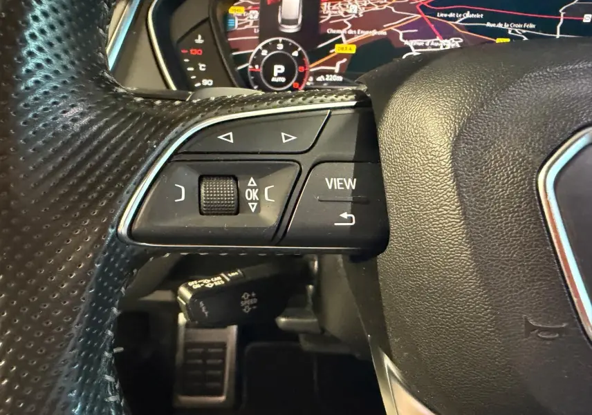 Gros plan sur le volant en cuir perforé de l'Audi Q5 Sportback gris, avec commandes multifonctions et affichage numérique du tableau de bord.