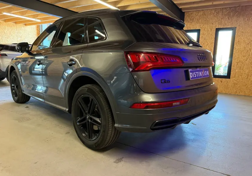 Audi Q5 Sportback gris vue 3/4 arrière droit en intérieur, avec jantes noires et feux arrière allumés.