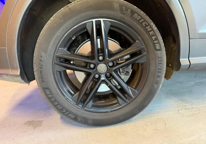 Gros plan sur la roue avant droite d'un Audi Q5 Sportback gris avec jante noire à cinq branches doubles.