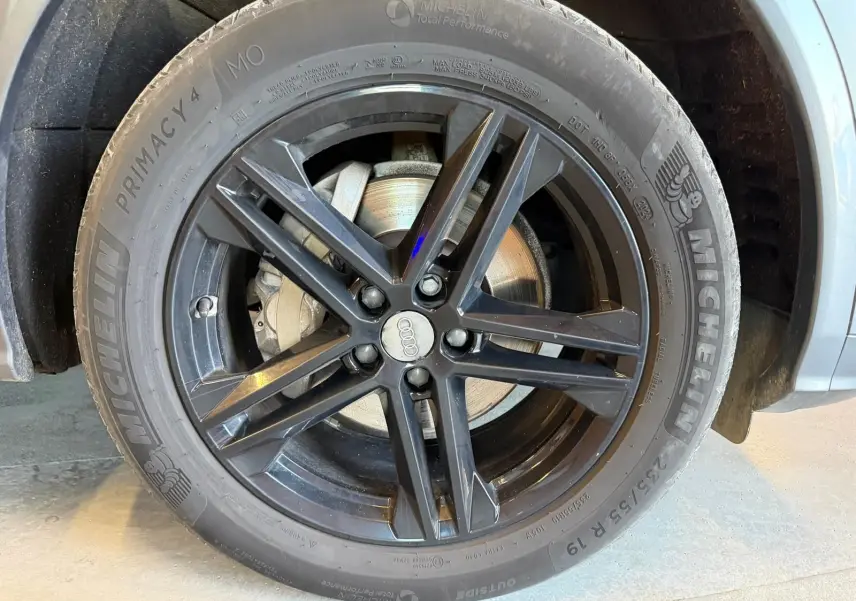 Gros plan sur la roue avant droite d’un Audi Q5 Sportback gris, jante alliage noir à 5 doubles branches.