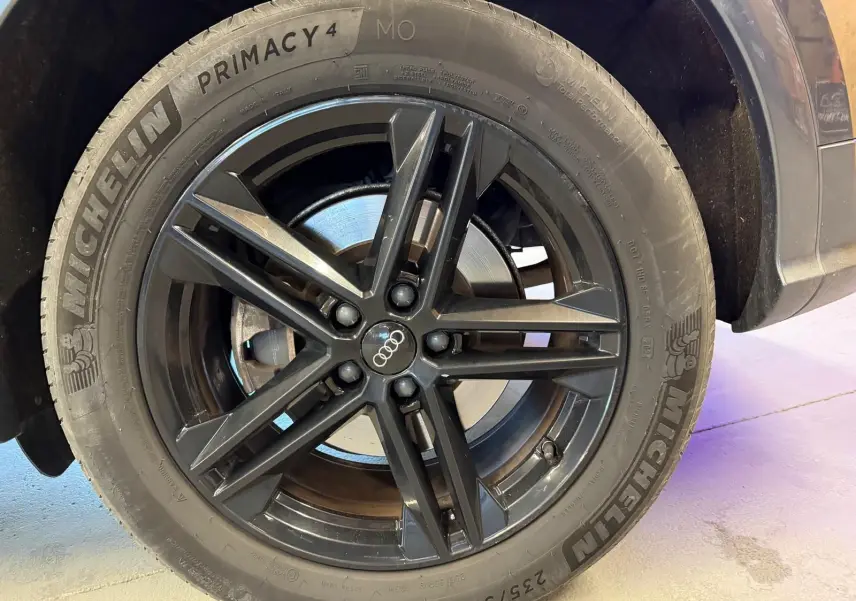 Gros plan sur la roue avant droite avec jante noire et pneu Michelin d’un Audi Q5 Sportback gris.