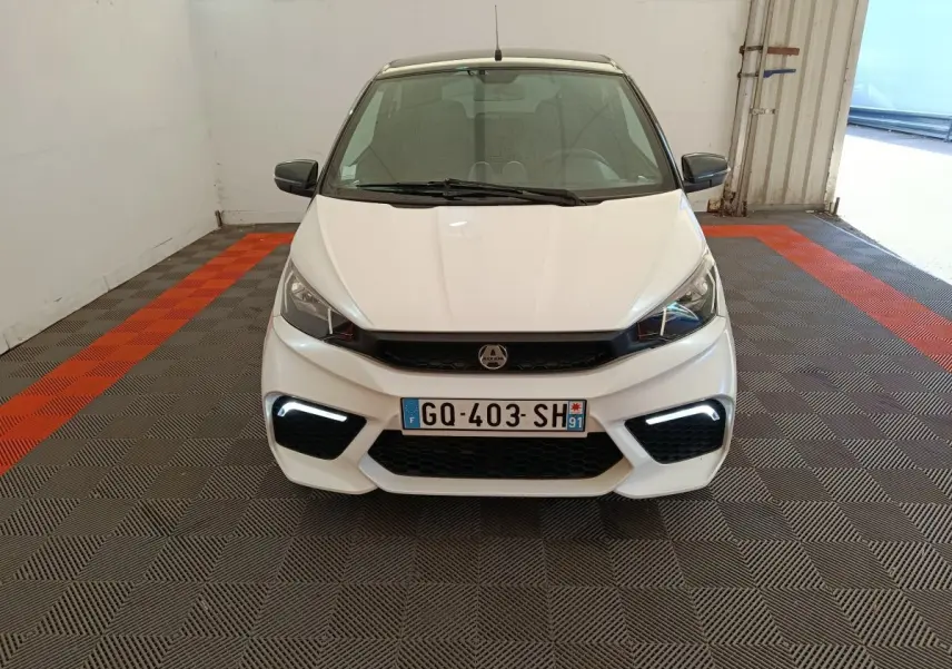 Vue de face d'une Aixam Ambition 0.5 City Coupe GTI blanche avec feux LED diurnes allumés dans un garage.