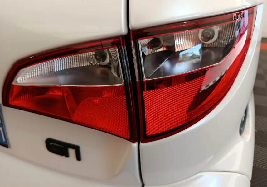 Gros plan sur les feux arrière rouges et blancs d'une Aixam Ambition 0.5 City Coupe GTI blanche, avec logo GT visible.