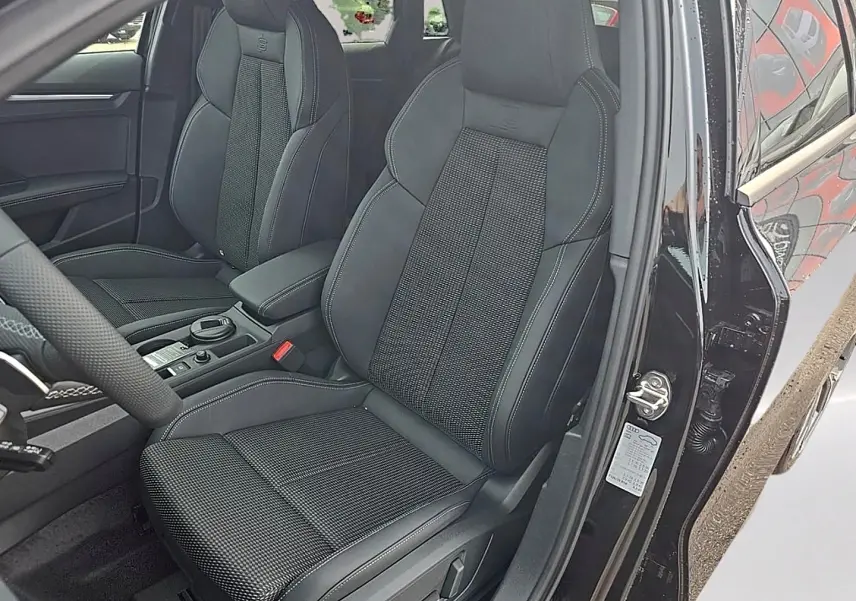 Vue intérieure côté conducteur de l'Audi A3 Sportback noir mythos, sièges sport avec surpiqûres blanches et accoudoir central.
