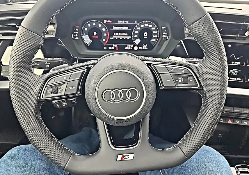 Vue rapprochée du volant sport en cuir noir perforé avec logo S d'une Audi A3 Sportback 2026, tableau de bord digital visible.