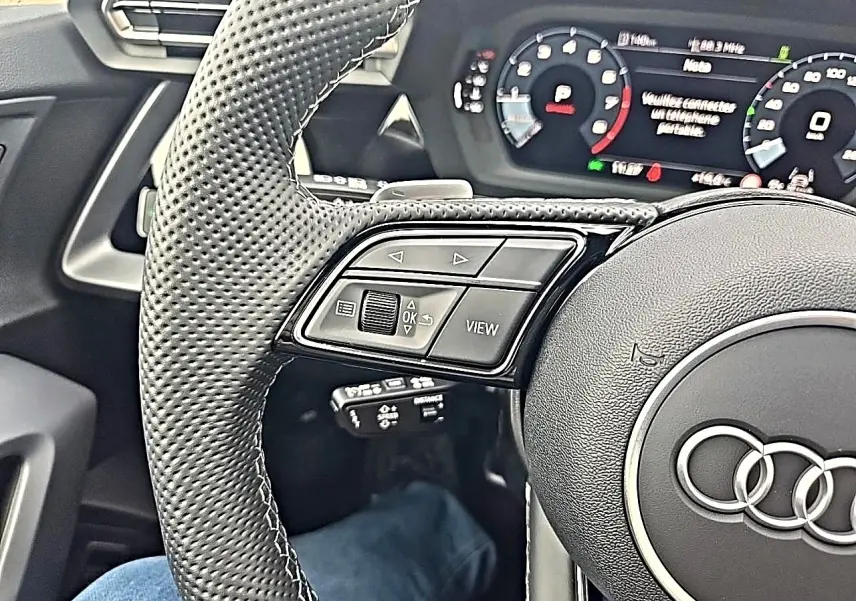 Gros plan sur le volant cuir perforé côté gauche de l’Audi A3 Sportback 2026 avec commandes multifonctions et tableau de bord digital.
