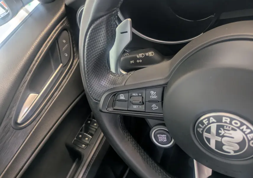 Gros plan sur le volant cuir noir de l'Alfa Romeo Stelvio blanc 2023 avec commandes de régulateur et bouton start/stop.