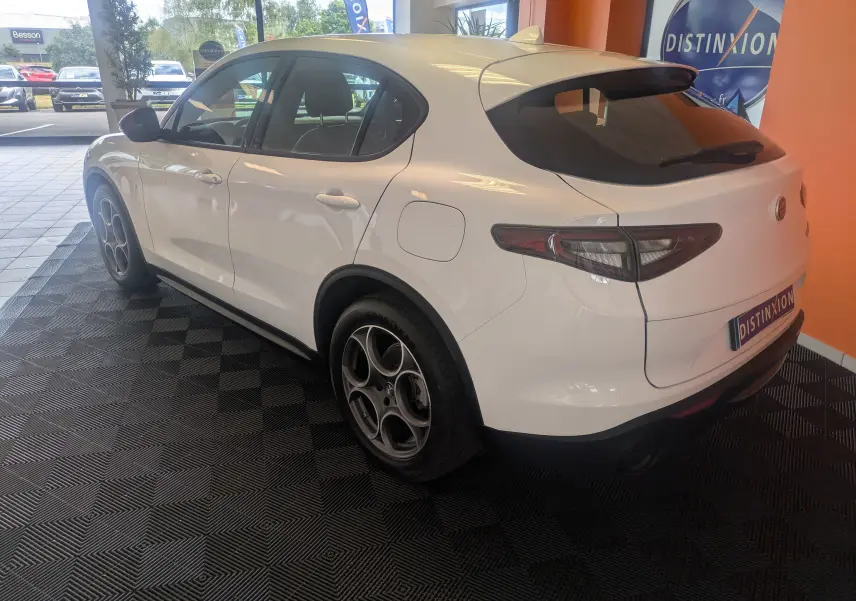 Vue 3/4 arrière droite d'un Alfa Romeo Stelvio blanc 2023, soulignant ses jantes distinctives et sa silhouette élégante.
