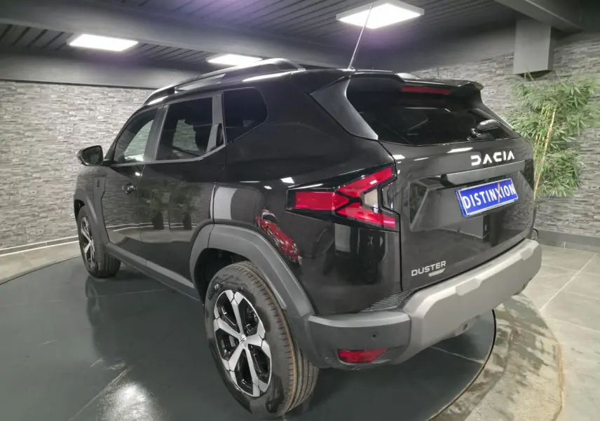 Vue 3/4 arrière droit du Dacia Duster 1.6 Hybrid noir nacré avec jantes alliage et barres de toit noires.