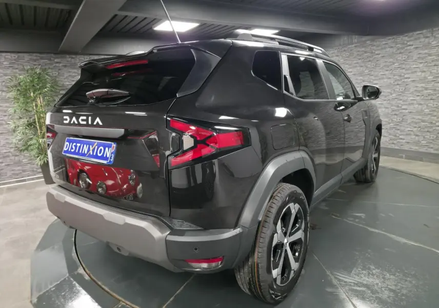 Vue 3/4 arrière droite du Dacia Duster 1.6 Hybrid noir nacré avec barres de toit et jantes alliage 18 pouces.