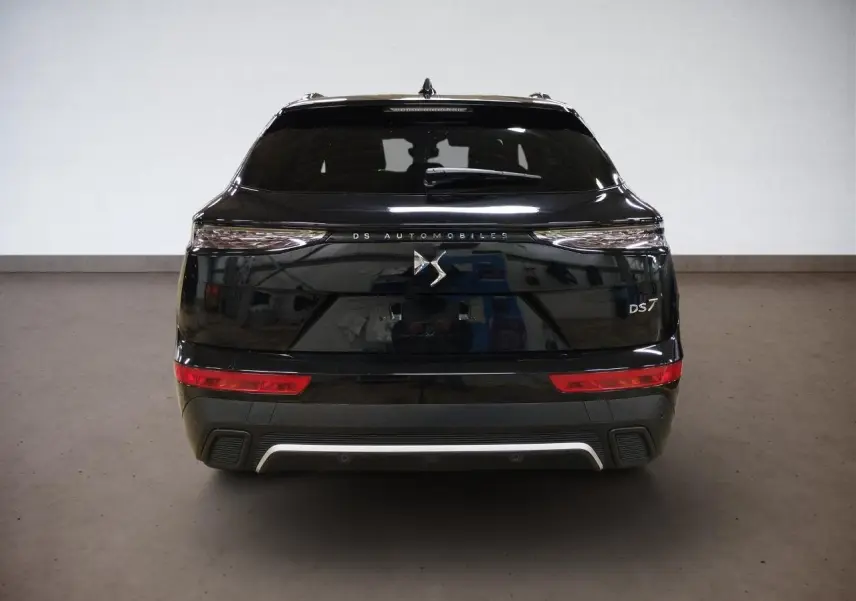 Vue arrière du DS7 noir Perla avec feux arrière 3D et logo DS centré sur le hayon dans un intérieur neutre.
