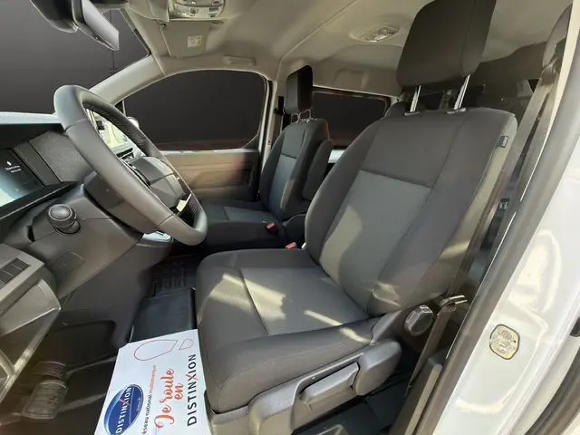 Vue intérieure côté conducteur du Citroën Jumpy cabine approfondie blanc, sièges tissu gris avec accoudoir et volant cuir.