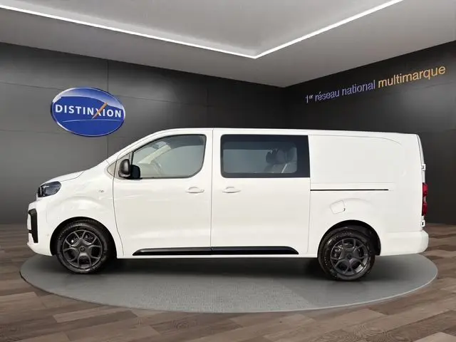 Vue de profil côté gauche d'un Citroën Jumpy cabine approfondie blanc Icy avec jantes alu noires, présenté en showroom.