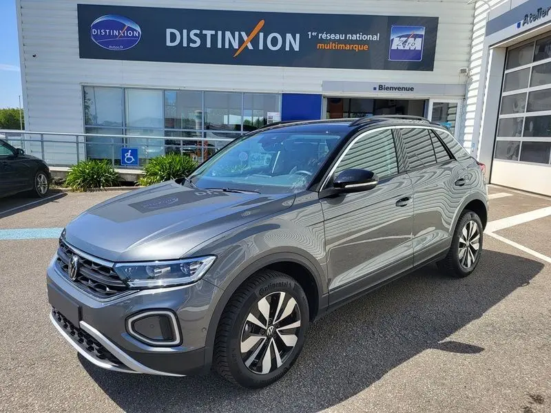 Volkswagen T-Roc gris Indium en 3/4 avant droit, avec attelage amovible visible, stationné devant un concessionnaire.