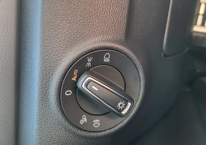 Gros plan sur le sélecteur de phares noir dans l'habitacle du Volkswagen T-Roc gris Indium, version 2025.