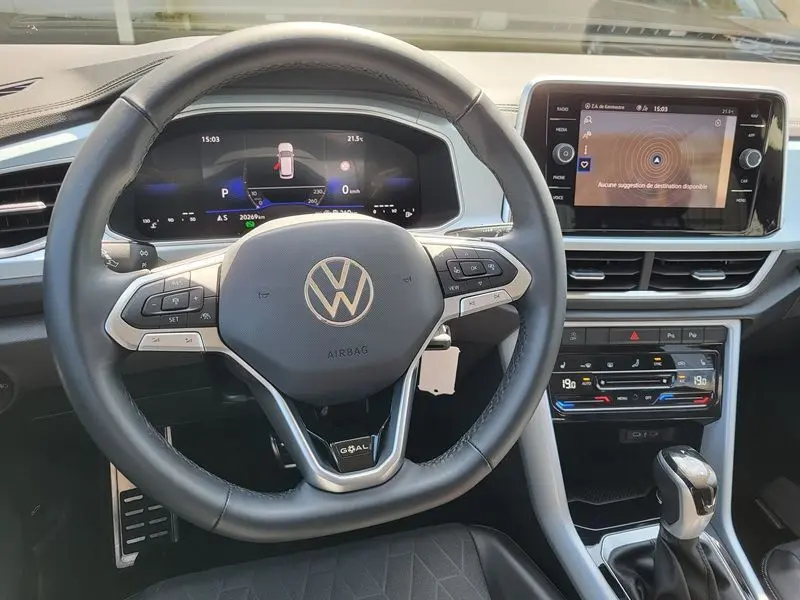Vue intérieure centrée sur le volant noir du Volkswagen T-Roc gris Indium, avec tableau de bord digital et écran tactile.